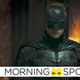 Robert Pattinson in his full Batman superhero suit stands in the middle of a crime scene.